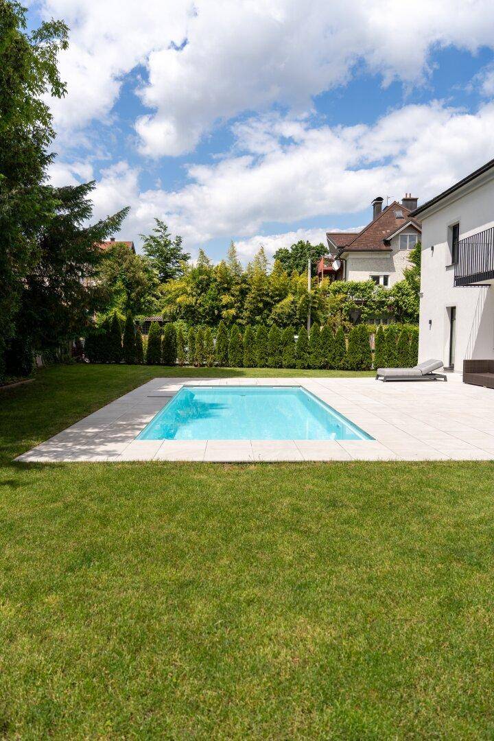 Gepflegter Gartenbereich mit rechteckigem Pool und weitläufiger Rasenfläche unter blauem Himmel.
