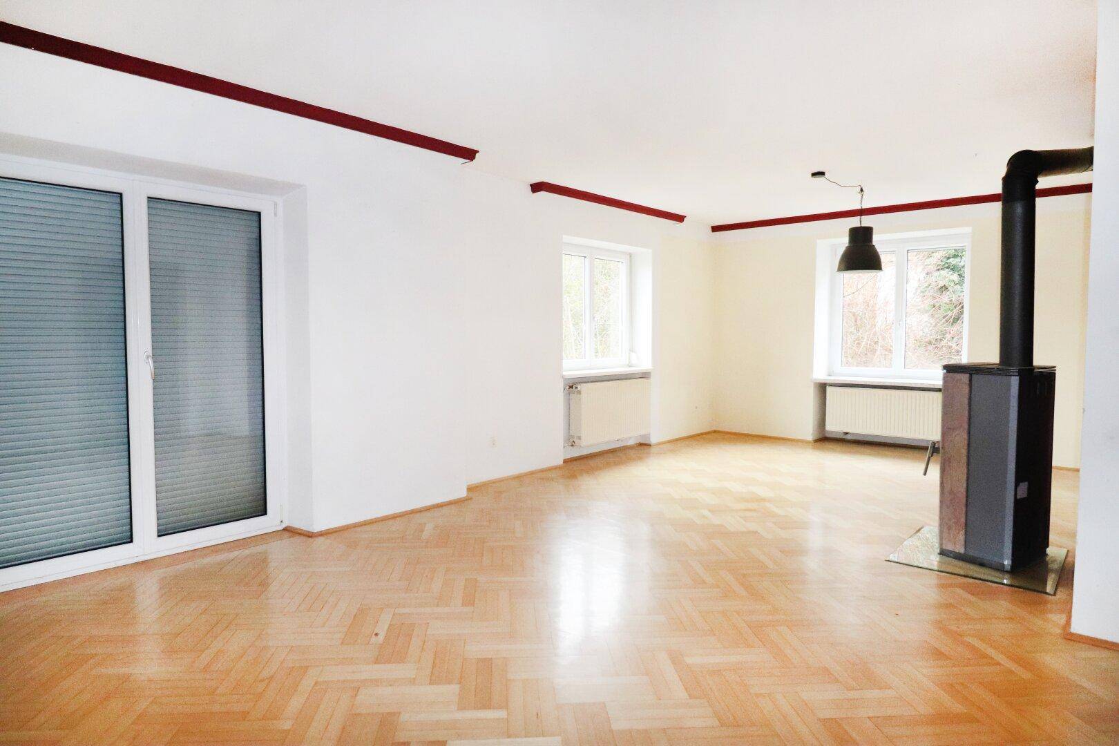 Helles Wohnzimmer mit Fischgrätparkett, einem modernen Holzofen und Zugang zum Außenbereich.