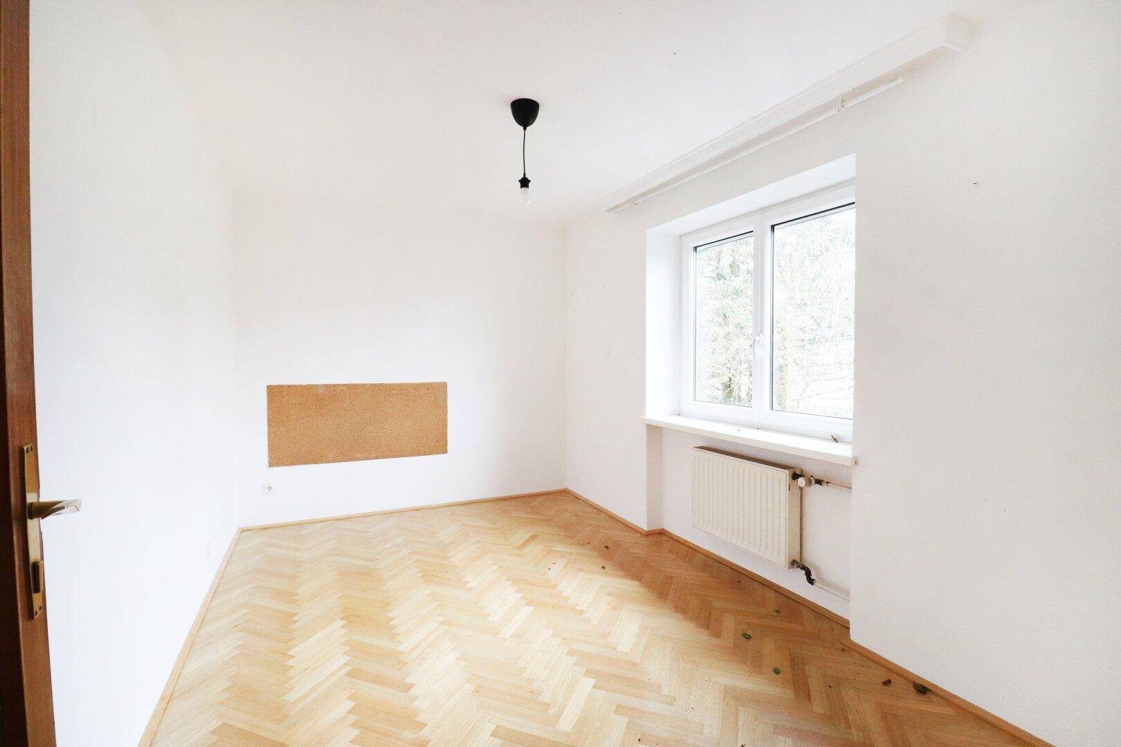 Helles Schlafzimmer mit Fischgrätparkett, weiß gestrichenen Wänden und einem Fenster.