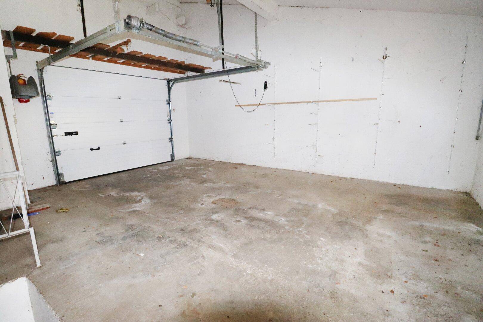 Geräumige Garage mit Betonboden, automatischem Tor und Stauraum an der Decke.