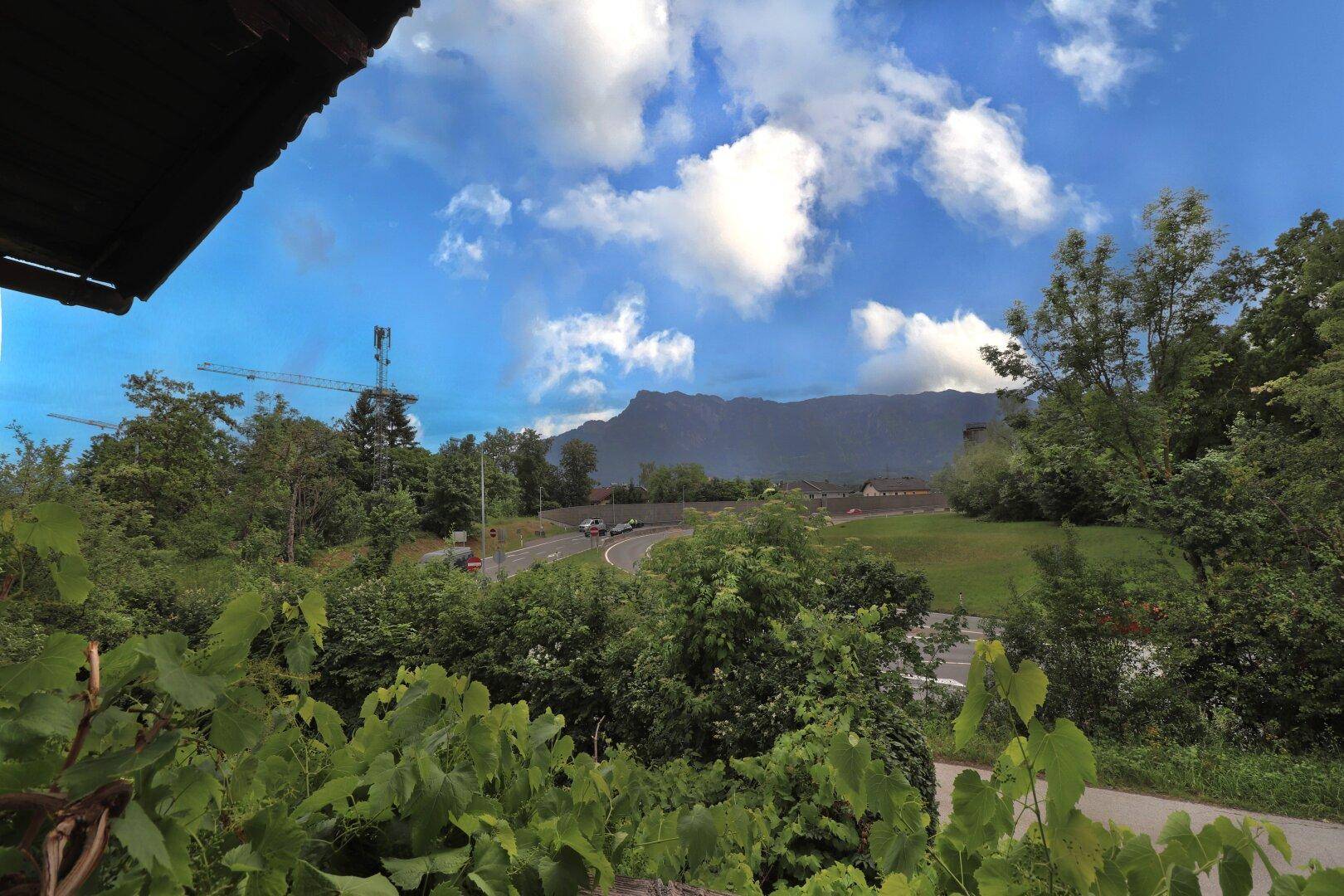 Weitläufiger Blick auf eine Berglandschaft und eine Straße, umgeben von üppigem Grün.
