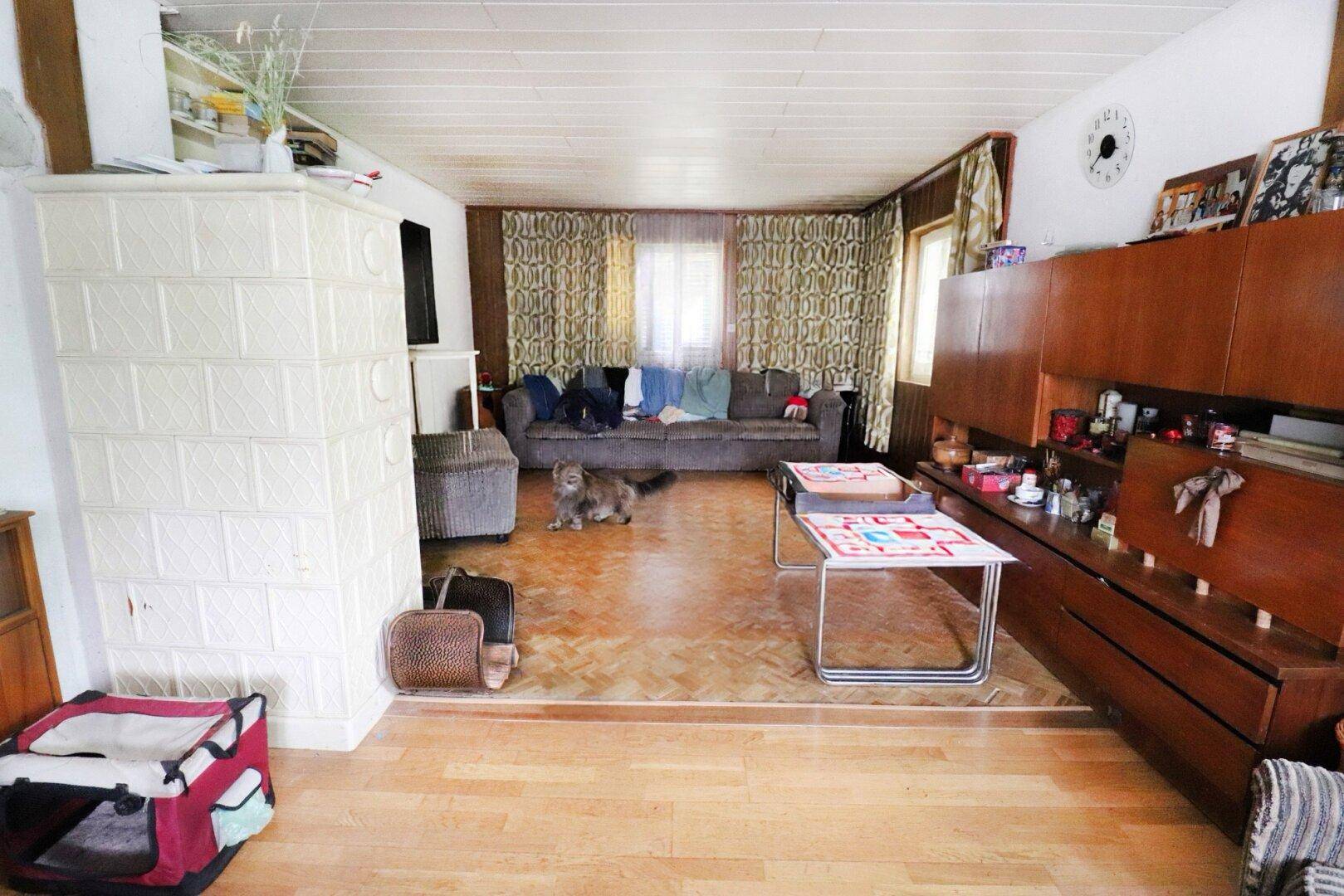 Gemütliches Wohnzimmer mit einem traditionellen Kachelofen, Holzfußboden und einem Sofa.