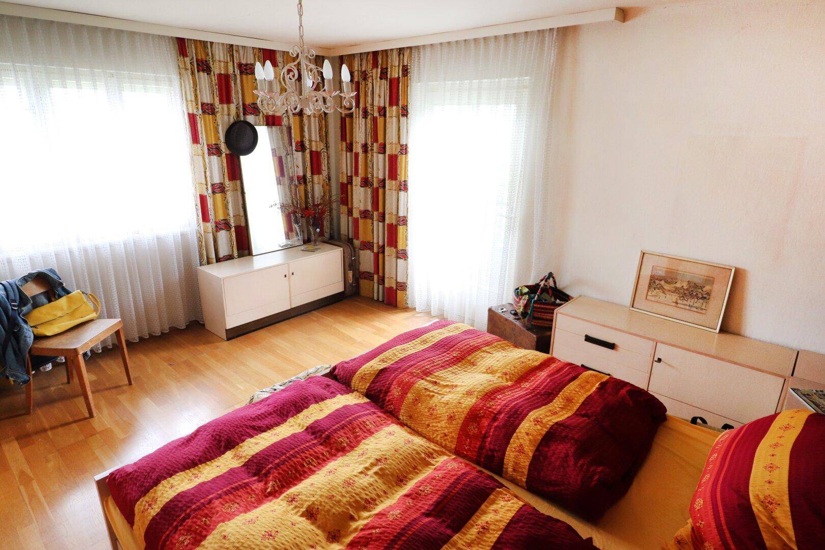 Schlafzimmer mit zwei Betten, bunten Vorhängen und hellem Holzfußboden.