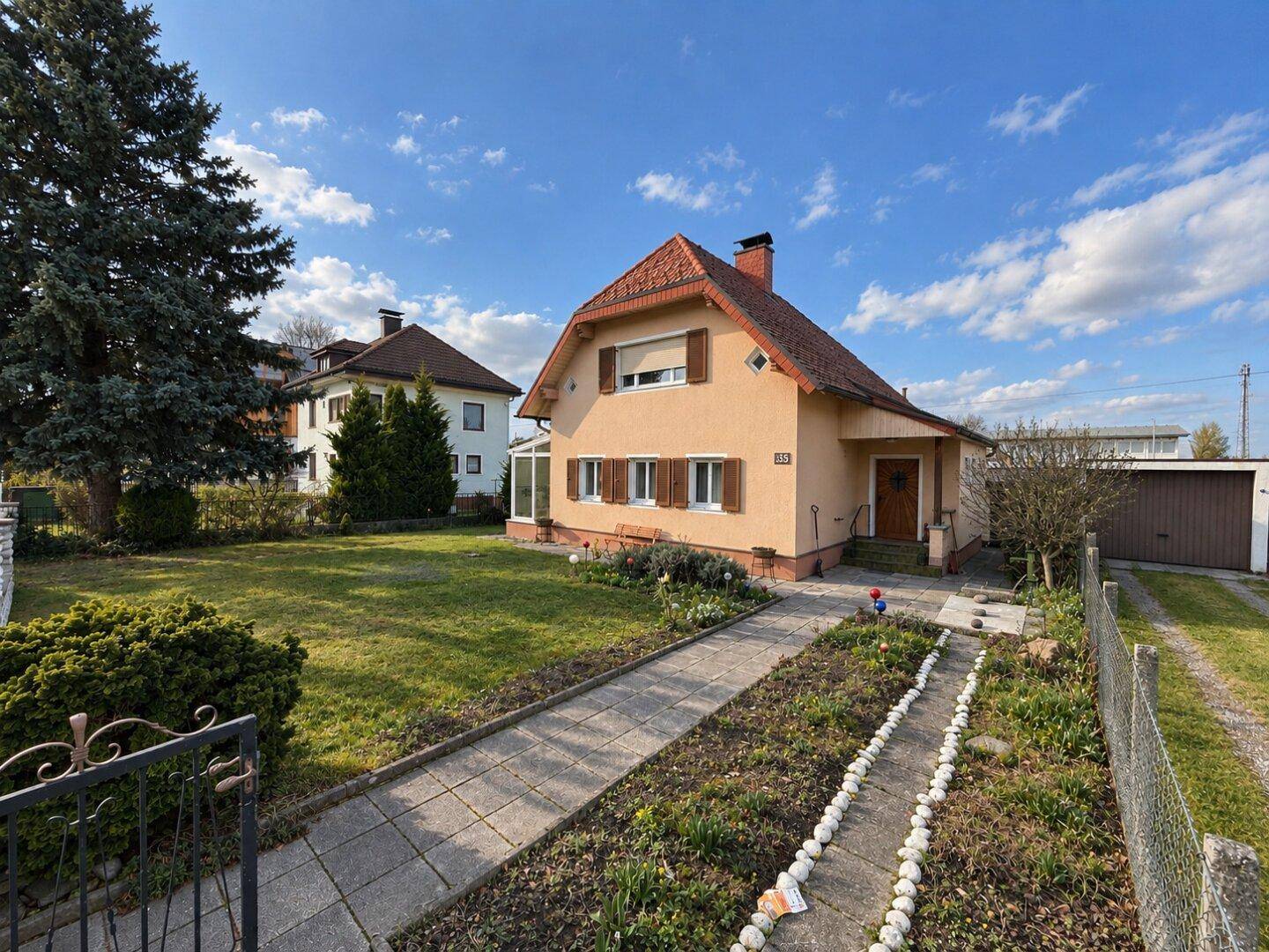Traditionelles Wohnhaus mit Satteldach, Rollläden und einem weitläufigen Garten mit Rasen und Bäumen.
