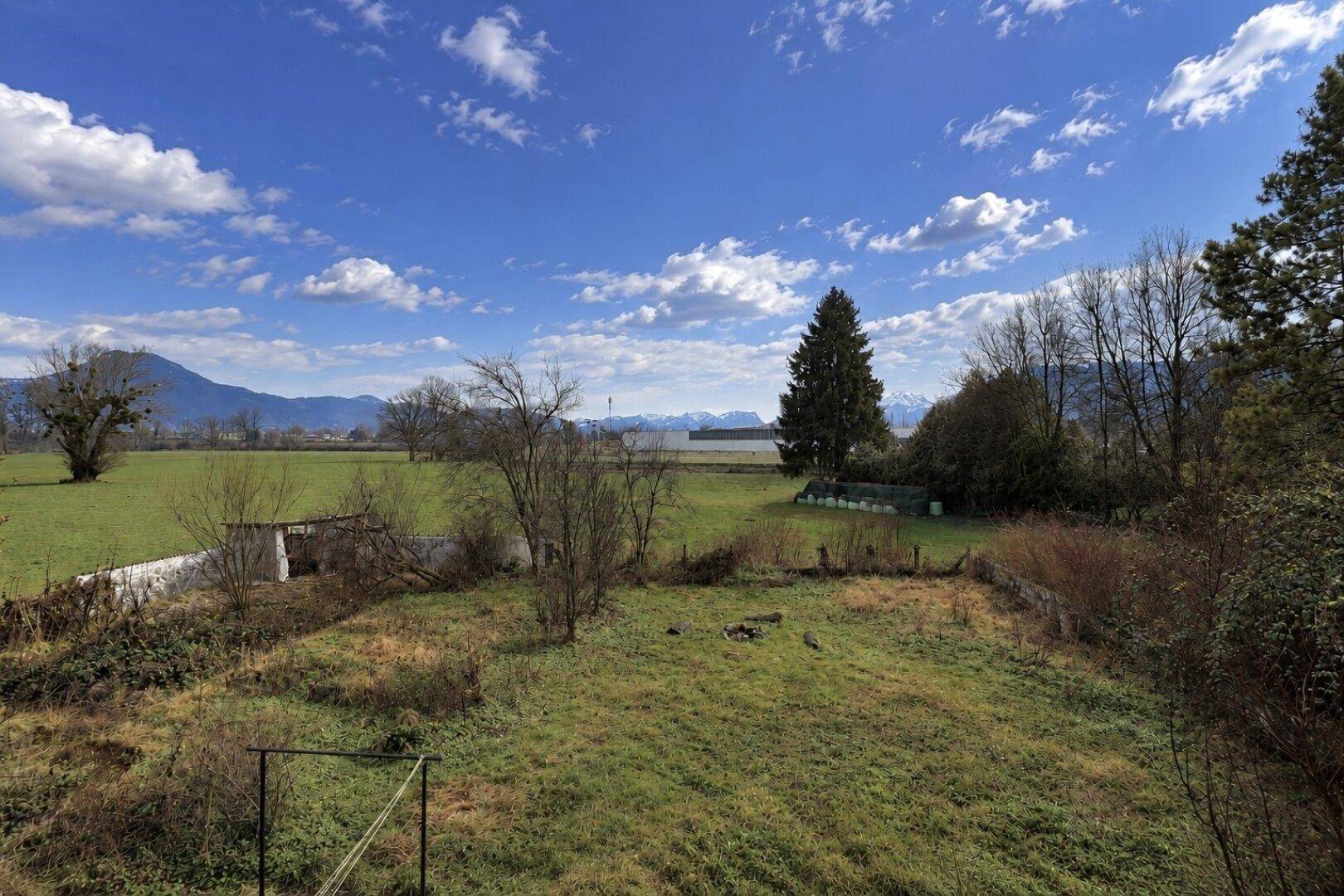 Weitläufiger Gartenbereich mit grüner Wiese, Bäumen und Blick auf die umliegende Landschaft und Berge.