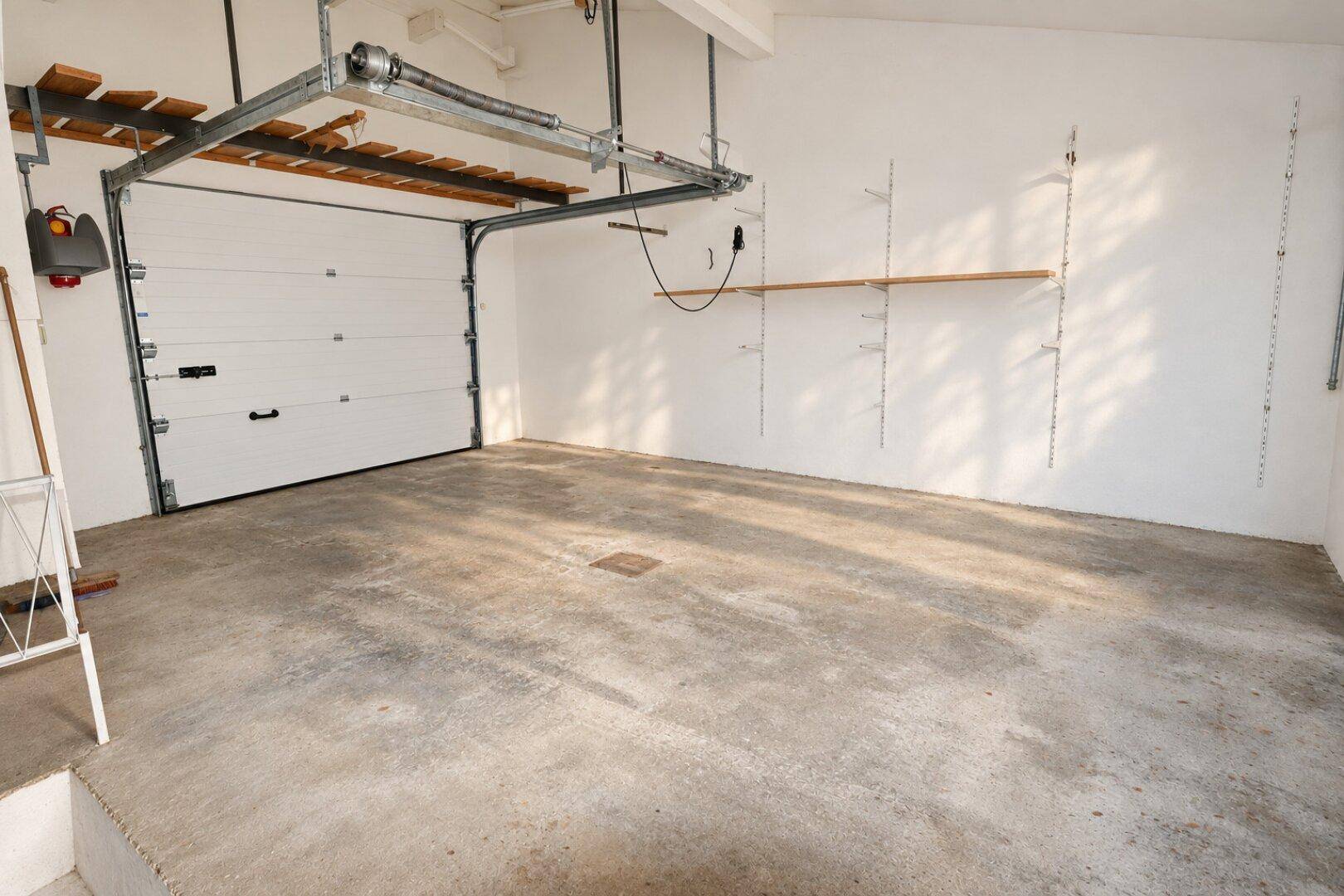 Geräumige Garage mit Betonboden, automatischem Tor und Regalsystemen für Stauraum.