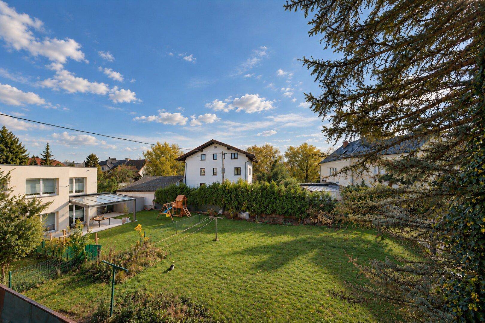 Weitläufiger Garten mit Spielplatz, umgeben von Hecken und weiteren Wohnhäusern.