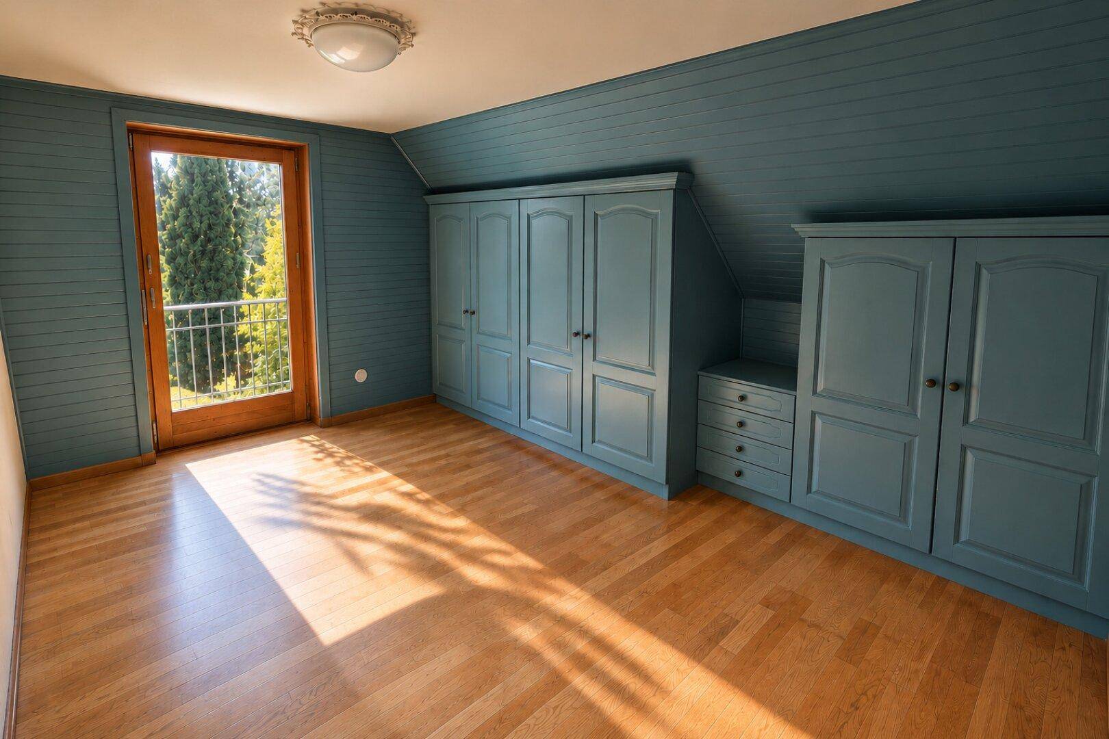 Gemütliches Schlafzimmer mit blauen Einbauschränken, Holzboden und Zugang zum Balkon.
