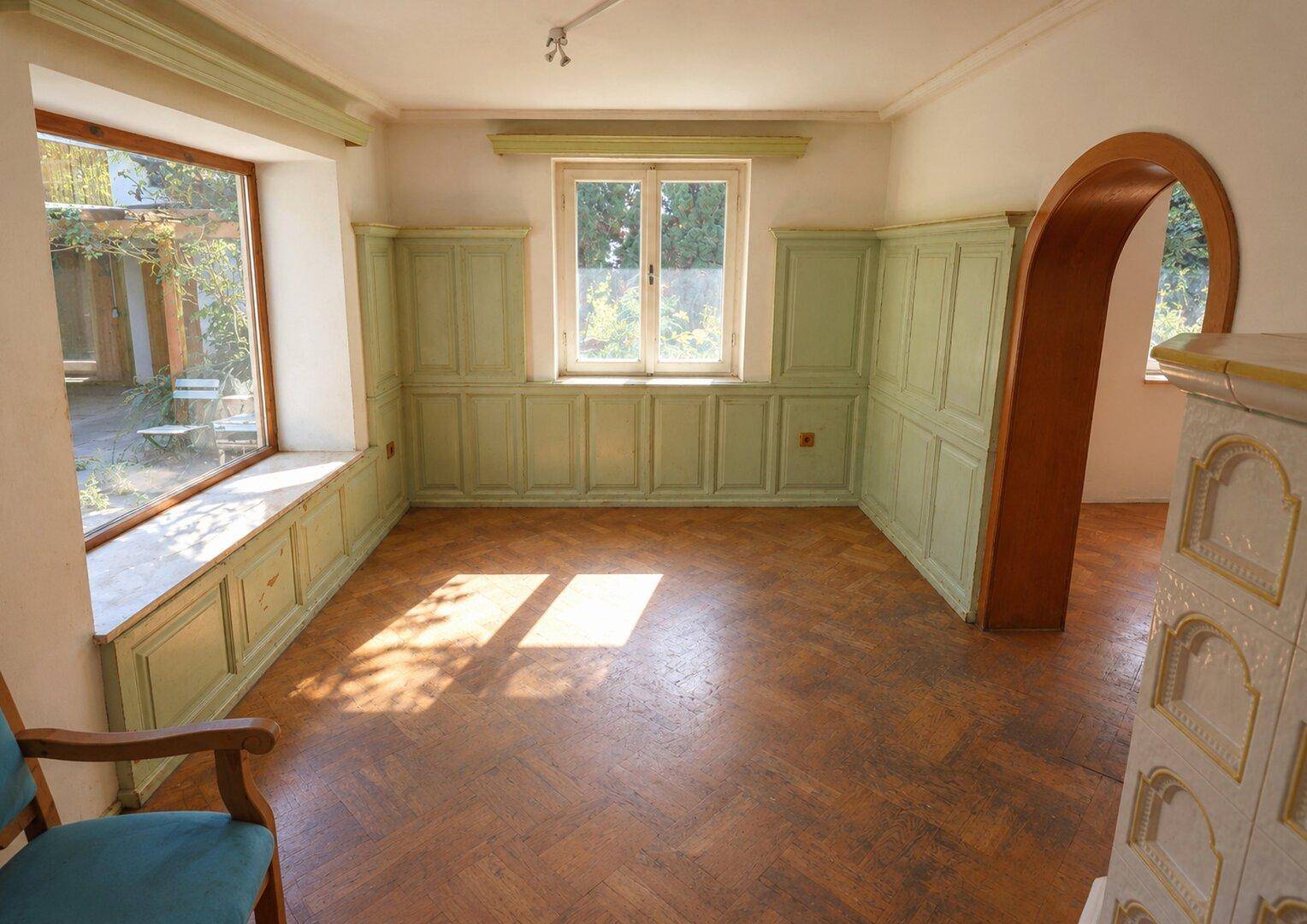 Heller Wohnraum mit Holzparkett, grüner Wandvertäfelung und traditionellem Kachelofen.