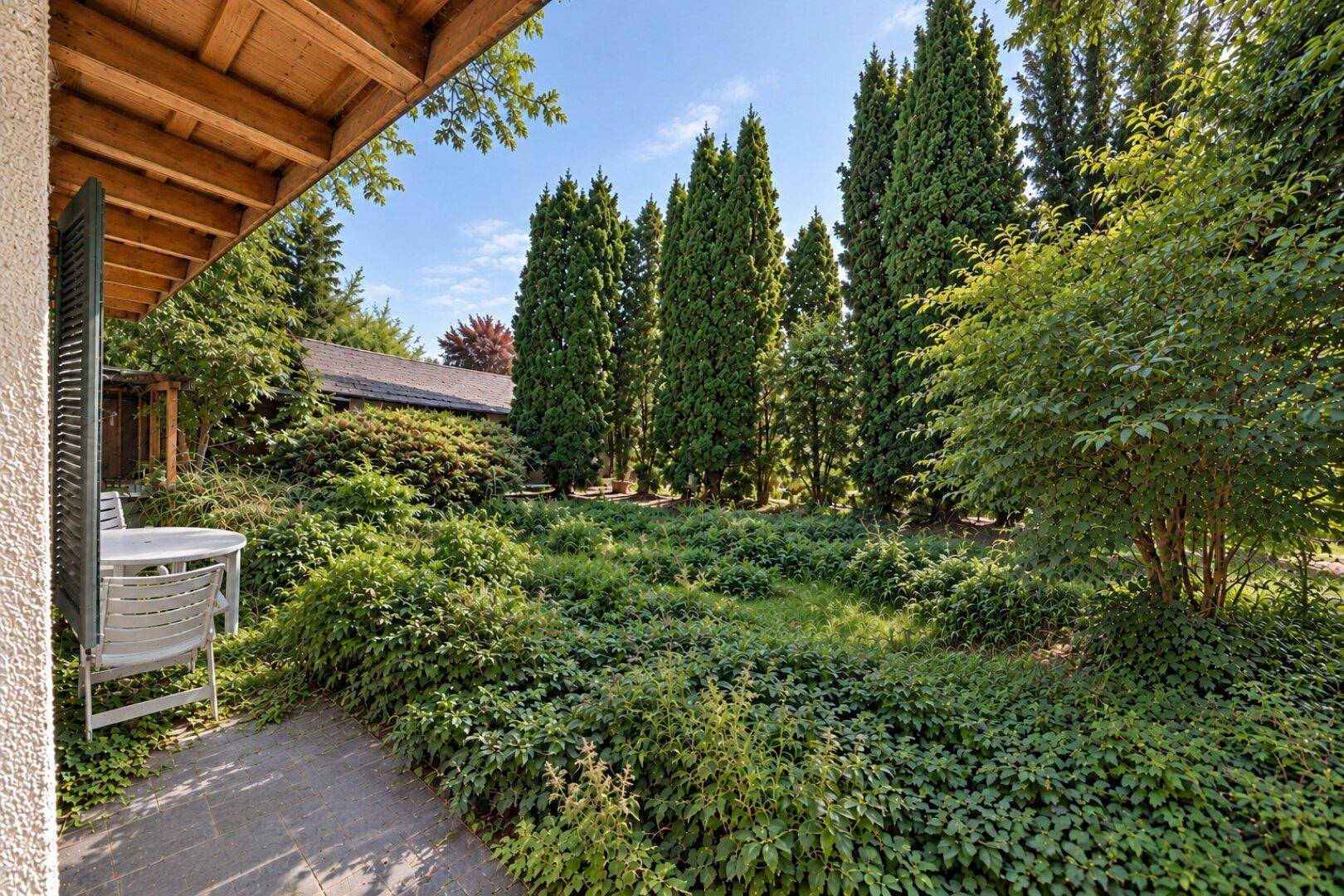 Ruhige Terrasse mit Gartenmöbeln und üppiger Bepflanzung, ideal zum Entspannen im Freien.