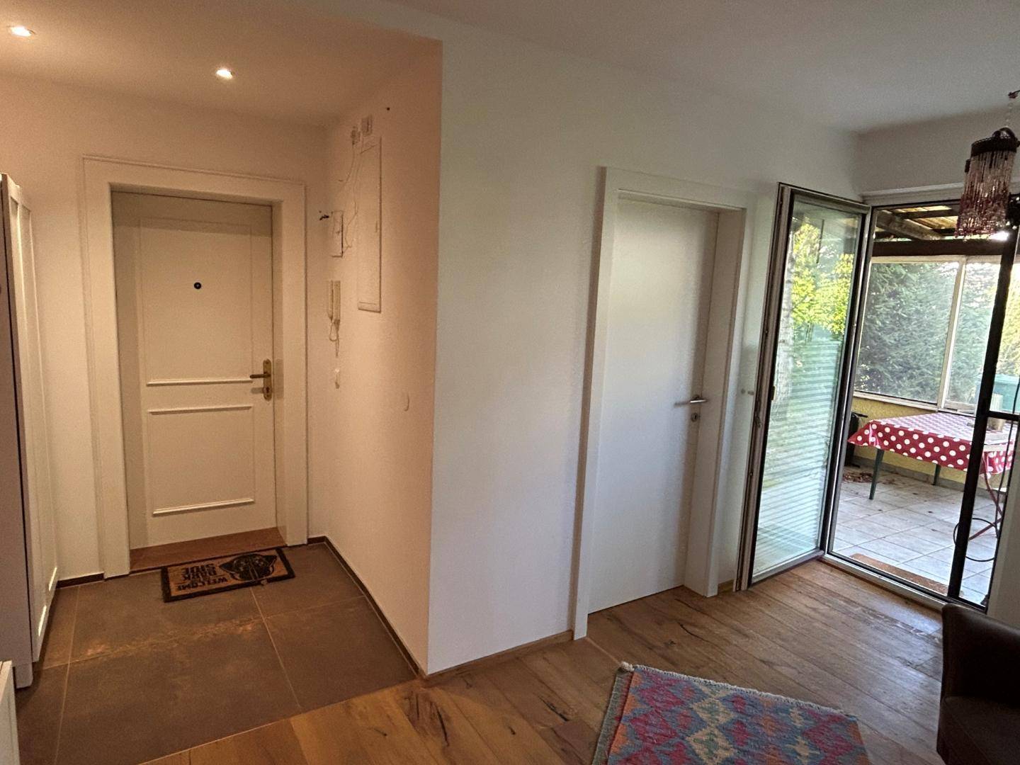 Eingangsbereich mit Holzboden und Zugang zu einem verglasten Außenbereich.
