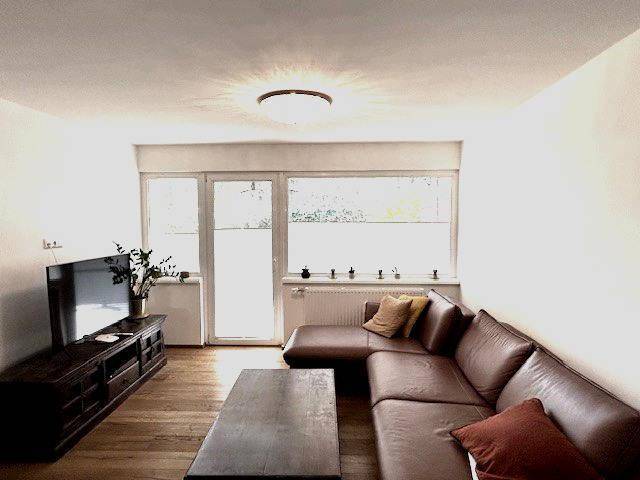 Gemütliches Wohnzimmer mit großem Ecksofa, Fernseher und Zugang zum Balkon.