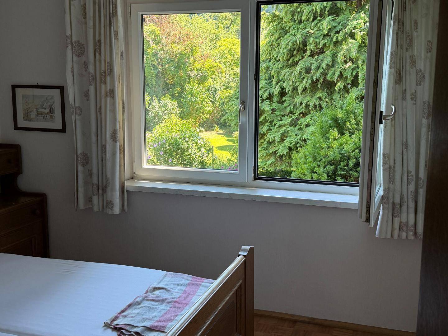 Schlafzimmer mit Holzbett und Fenster, das einen Blick ins Grüne bietet.