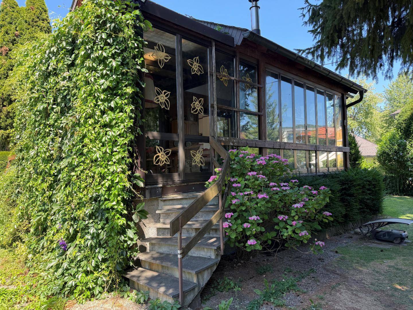 Verglaster Wintergarten mit üppiger Begrünung und Zugang zum Gartenbereich.