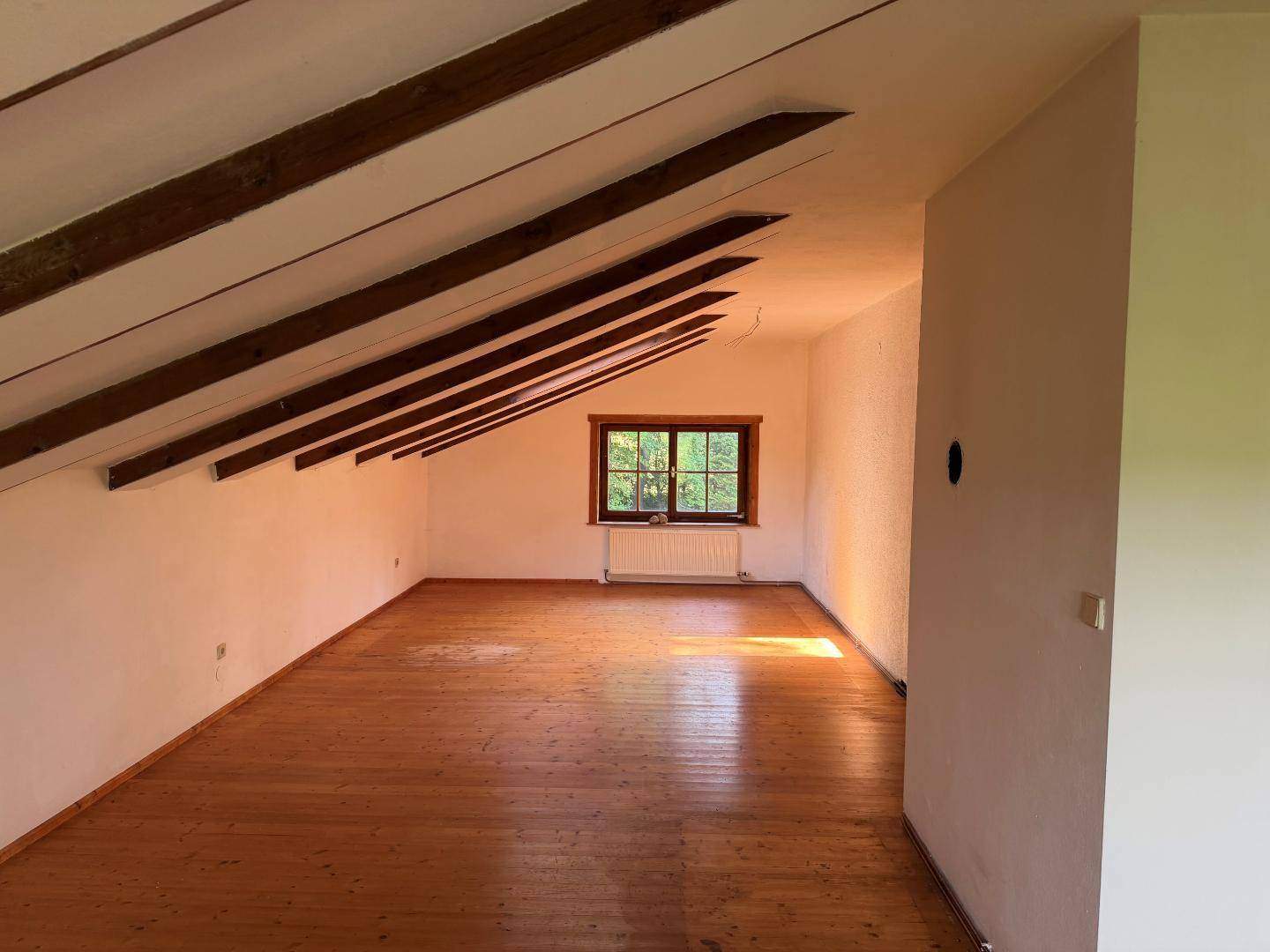 Helles Dachzimmer mit sichtbaren Holzbalken und Holzboden, ideal als Schlaf- oder Arbeitsbereich.