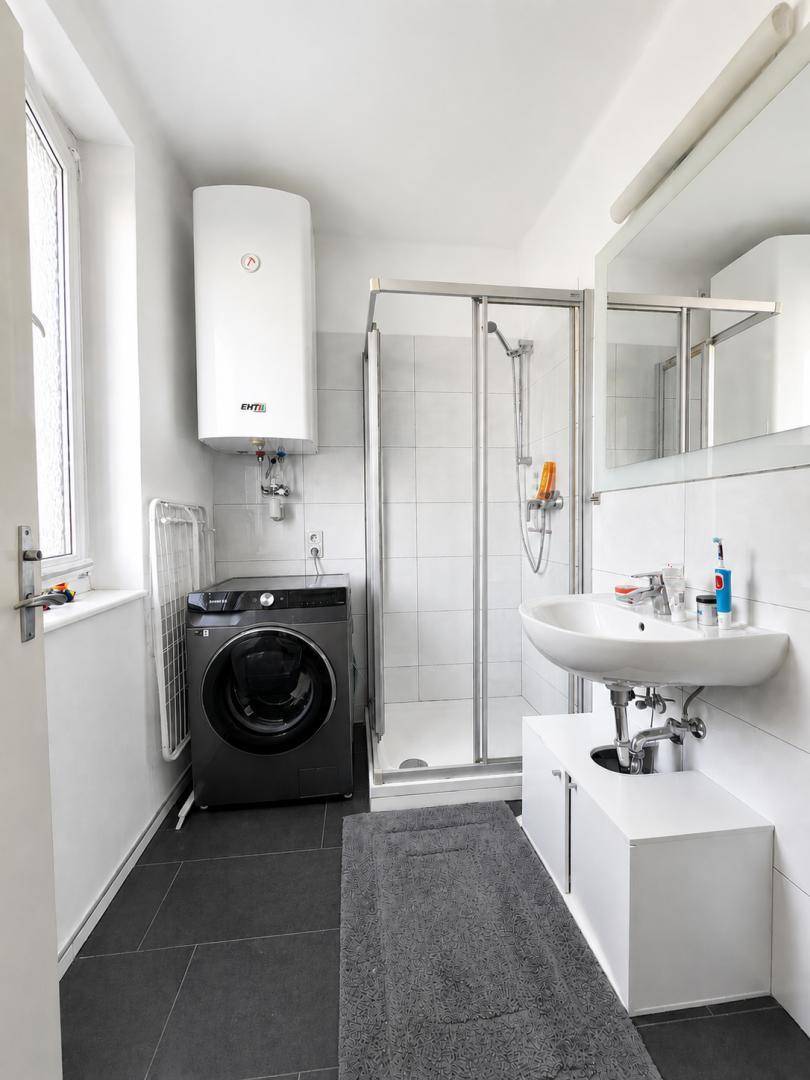 Modernes Badezimmer mit Dusche, Waschbecken, Waschmaschine, Spiegelschrank und Fenster.