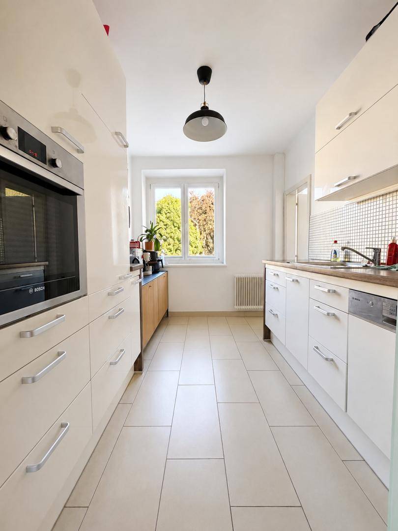 Moderne Küche mit weißen Hochglanzfronten, integriertem Backofen, Spülmaschine und Fenster.