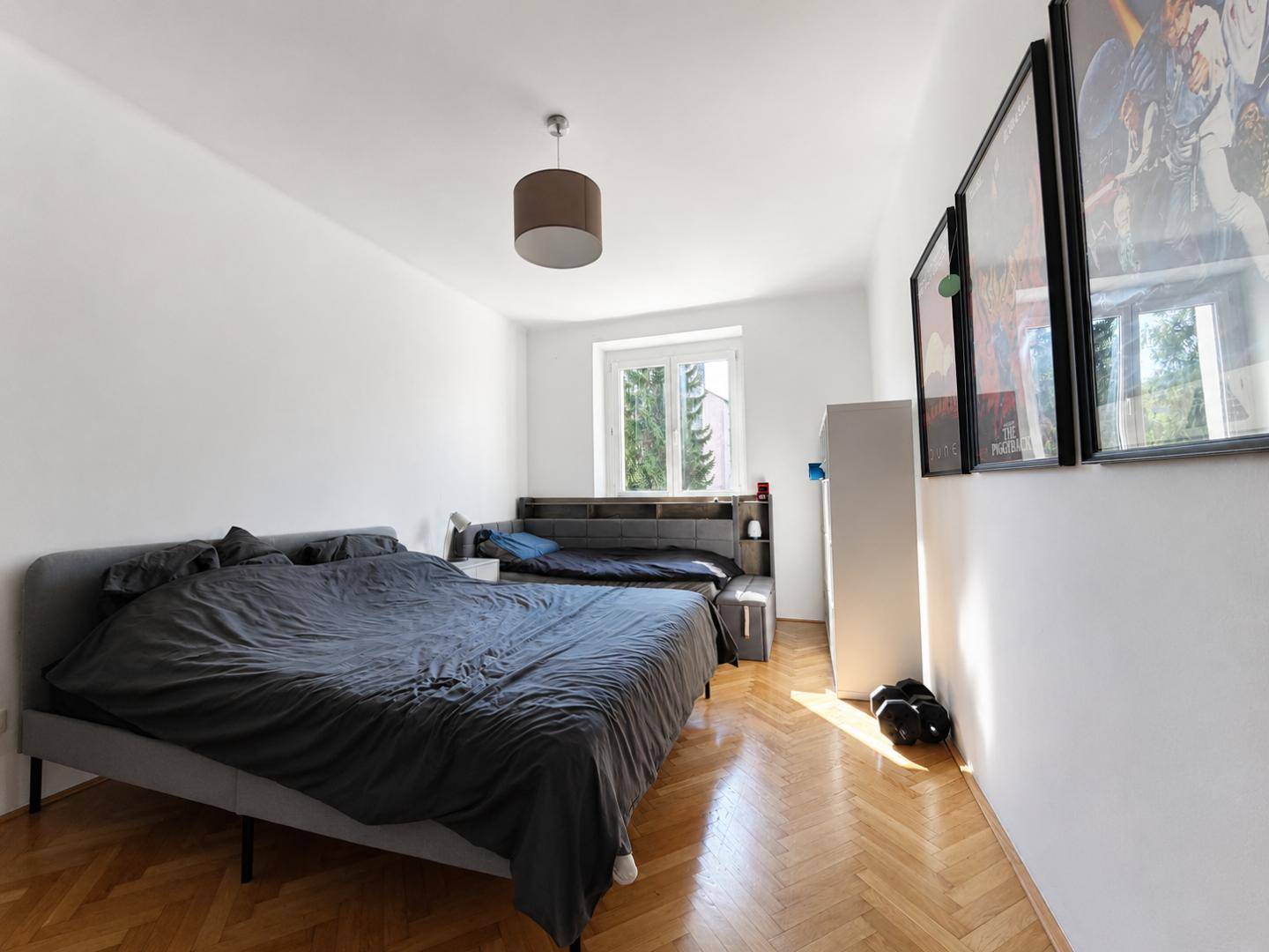 Schlafzimmer mit Parkettboden, großem Bett und Fenster mit Blick ins Grüne.