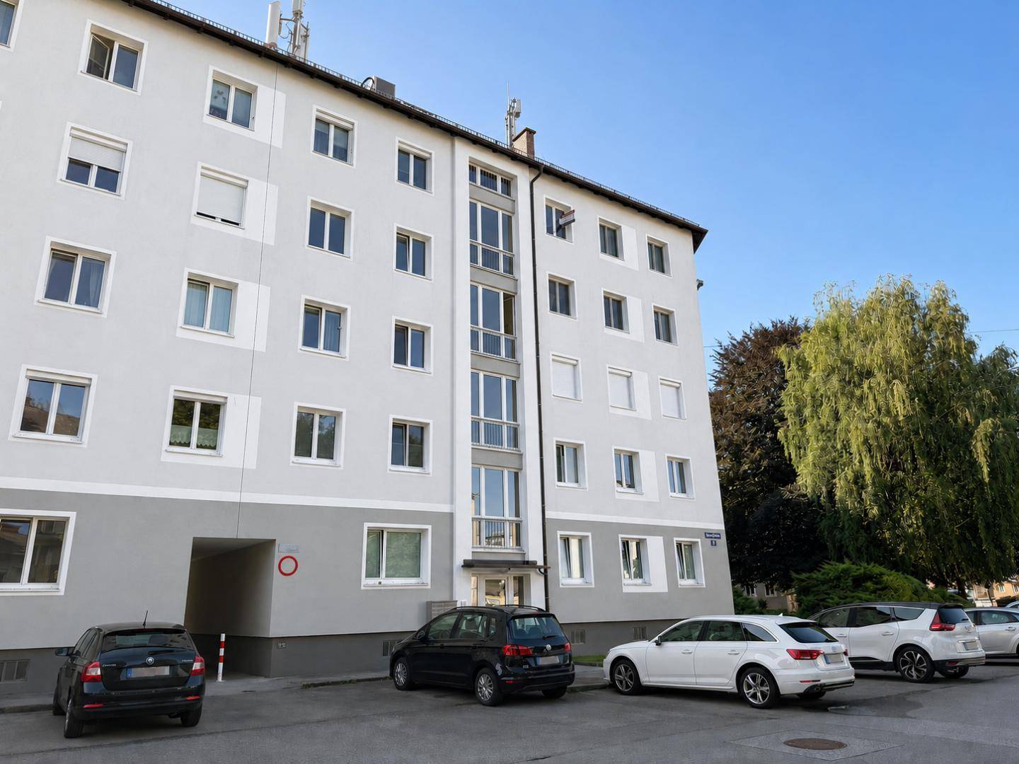 Mehrfamilienhaus mit moderner Fassade, vielen Fenstern und Parkplätzen davor.