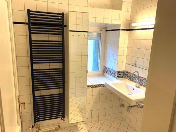 Modernes Badezimmer mit weißen Fliesen, Waschbecken und einem beheizten Handtuchhalter.