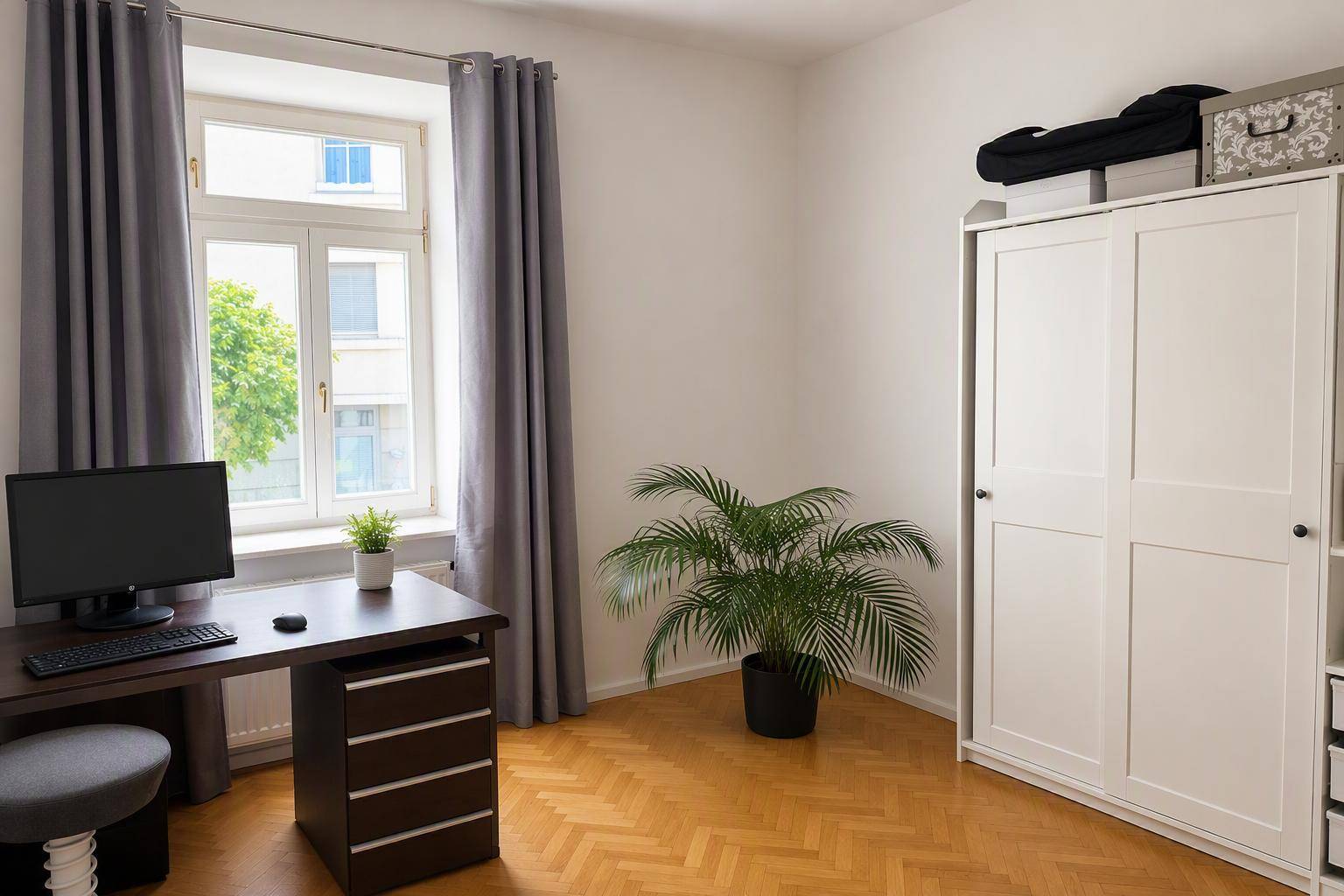 Helles Arbeitszimmer mit Schreibtisch, weißem Kleiderschrank und Blick ins Grüne.
