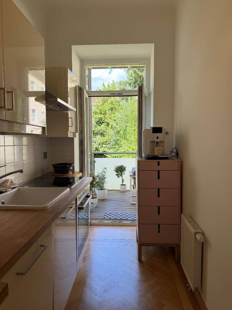 Kleine Küche mit Holztheke, weißen Hochglanzfronten und Zugang zu einem Balkon.