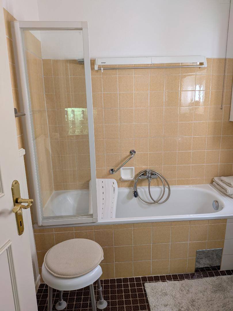 Badezimmer mit Badewanne, Duschabtrennung und beigefarbenen Fliesen im Stil der 80er Jahre.