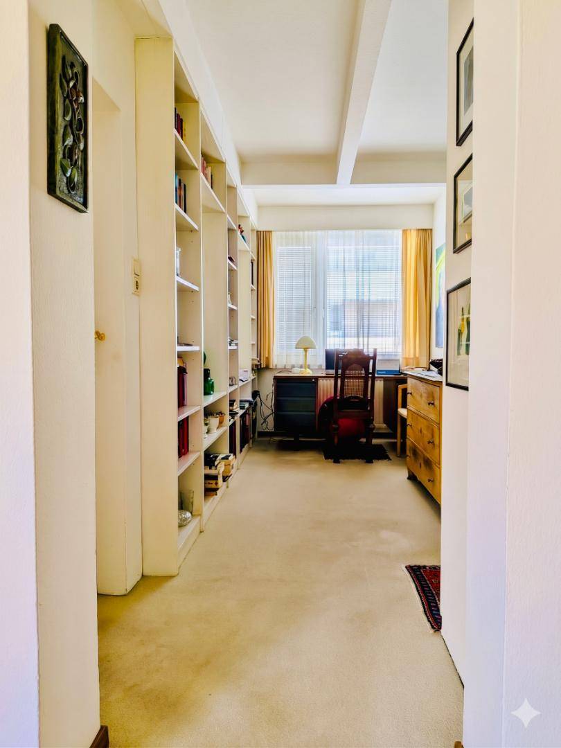 Langer Flur mit integrierten Bücherregalen, der zu einem hellen Arbeitsbereich mit Schreibtisch führt.