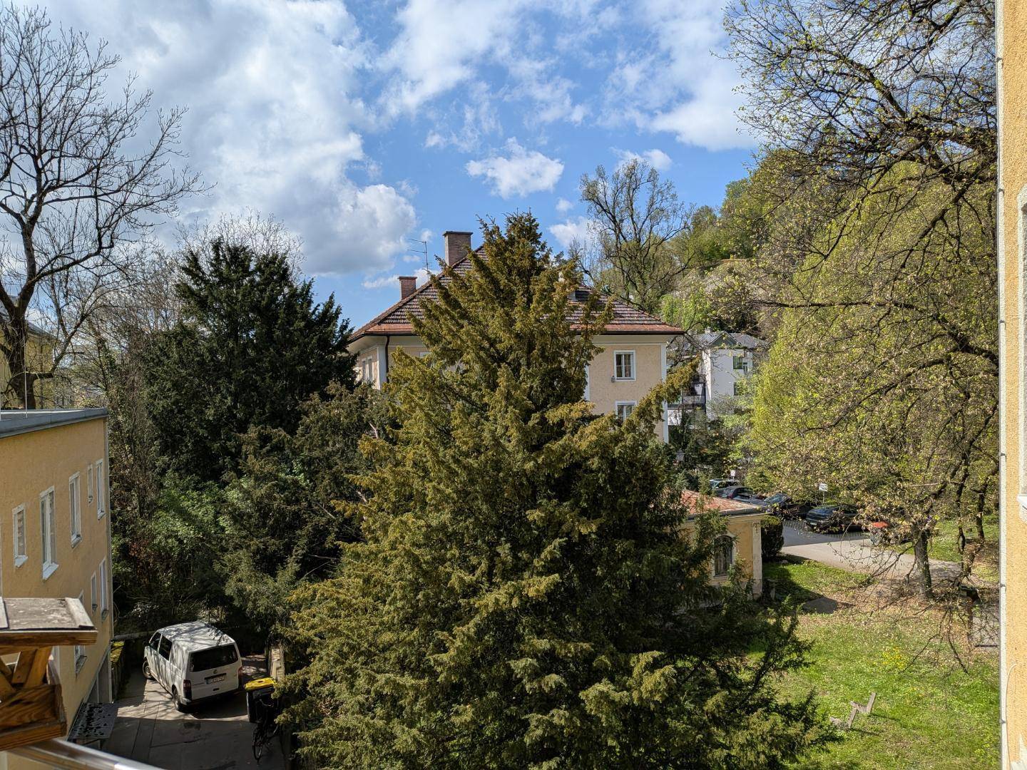 Blick auf grüne Bäume und umliegende Gebäude unter einem blauen Himmel mit weißen Wolken.