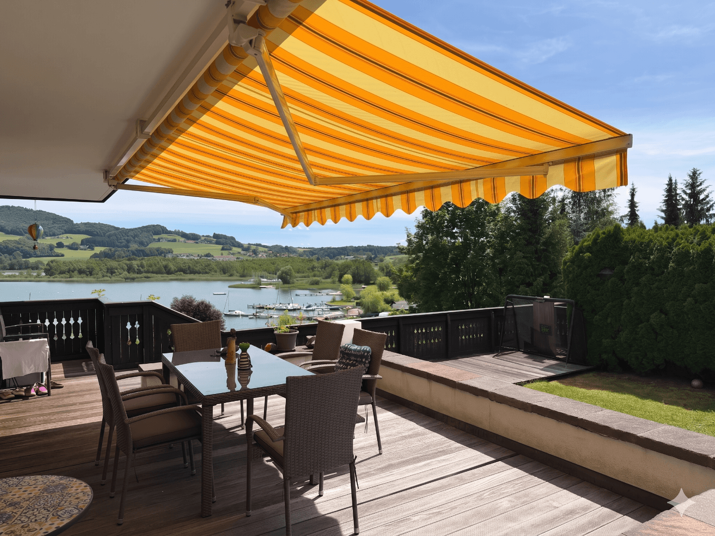 Gemütliche Terrasse mit gestreifter Markise, Esstisch und weitem Blick auf den See und die Landschaft.