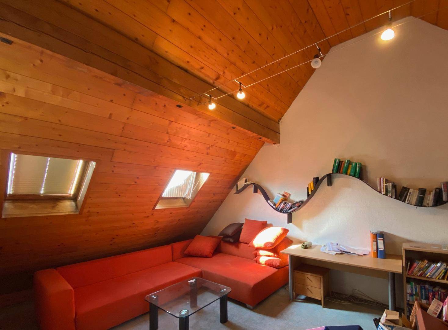Gemütliches Dachzimmer mit Holzverkleidung, Dachfenstern und Bücherregalen.