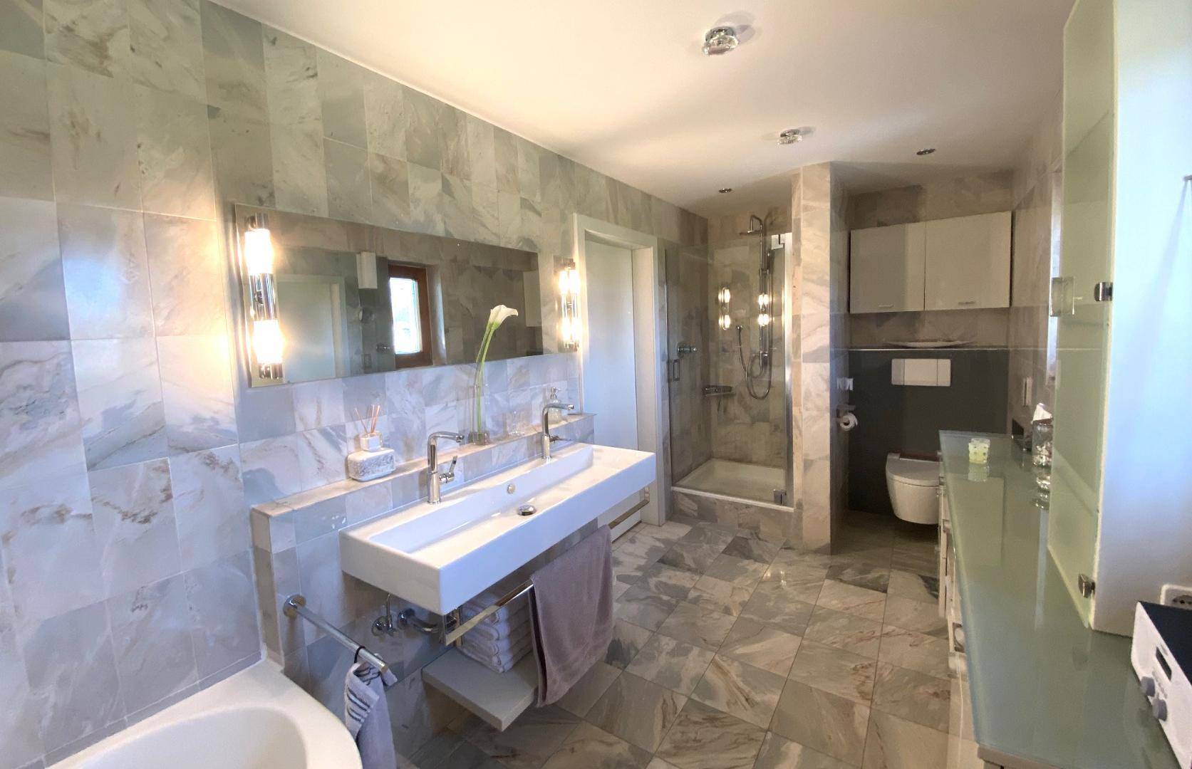Modernes Badezimmer mit doppelten Waschbecken, großer Dusche und Marmorfliesen.