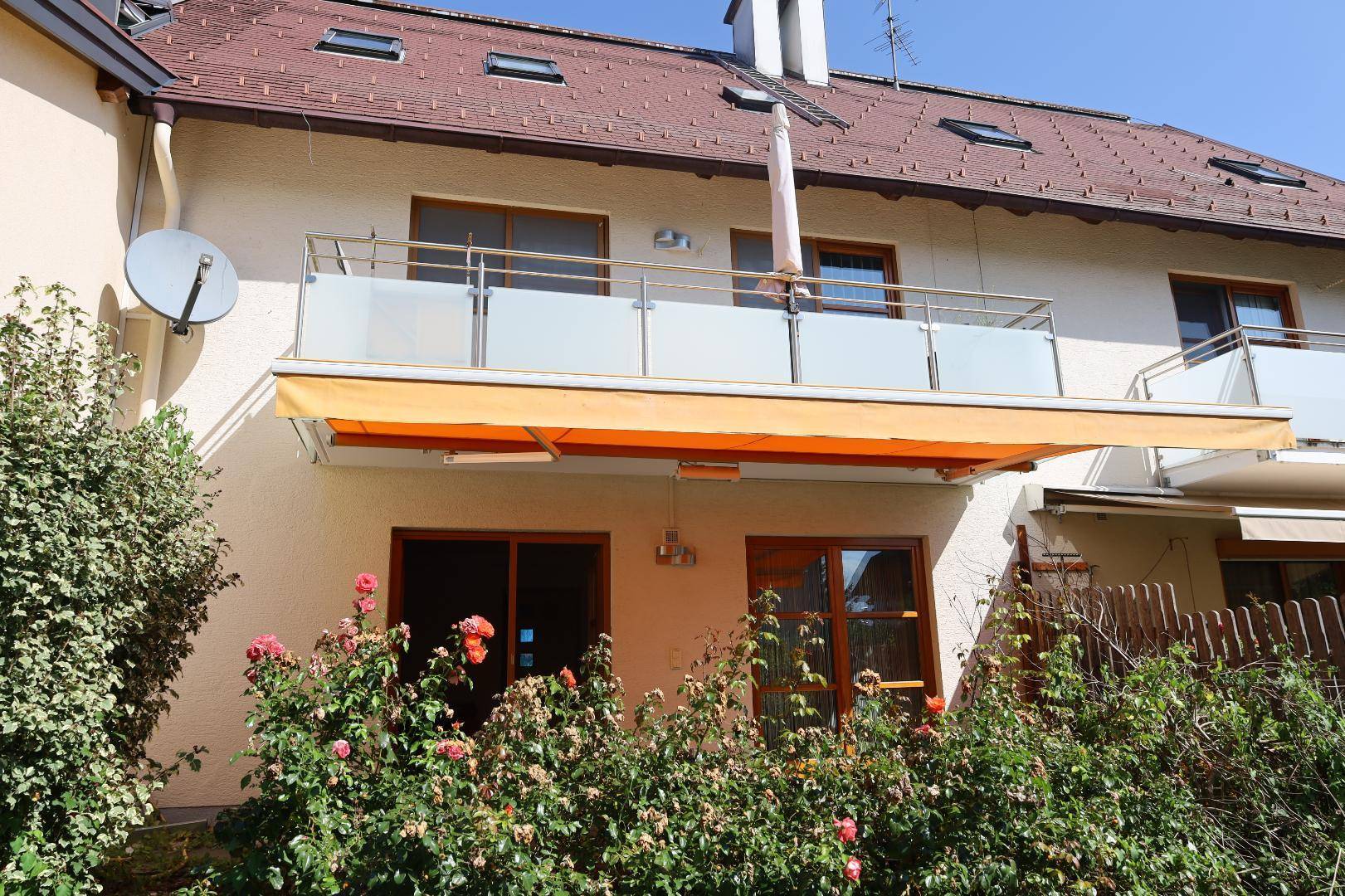 Balkon mit orangefarbener Markise und Glasgeländer an der Hausfassade.