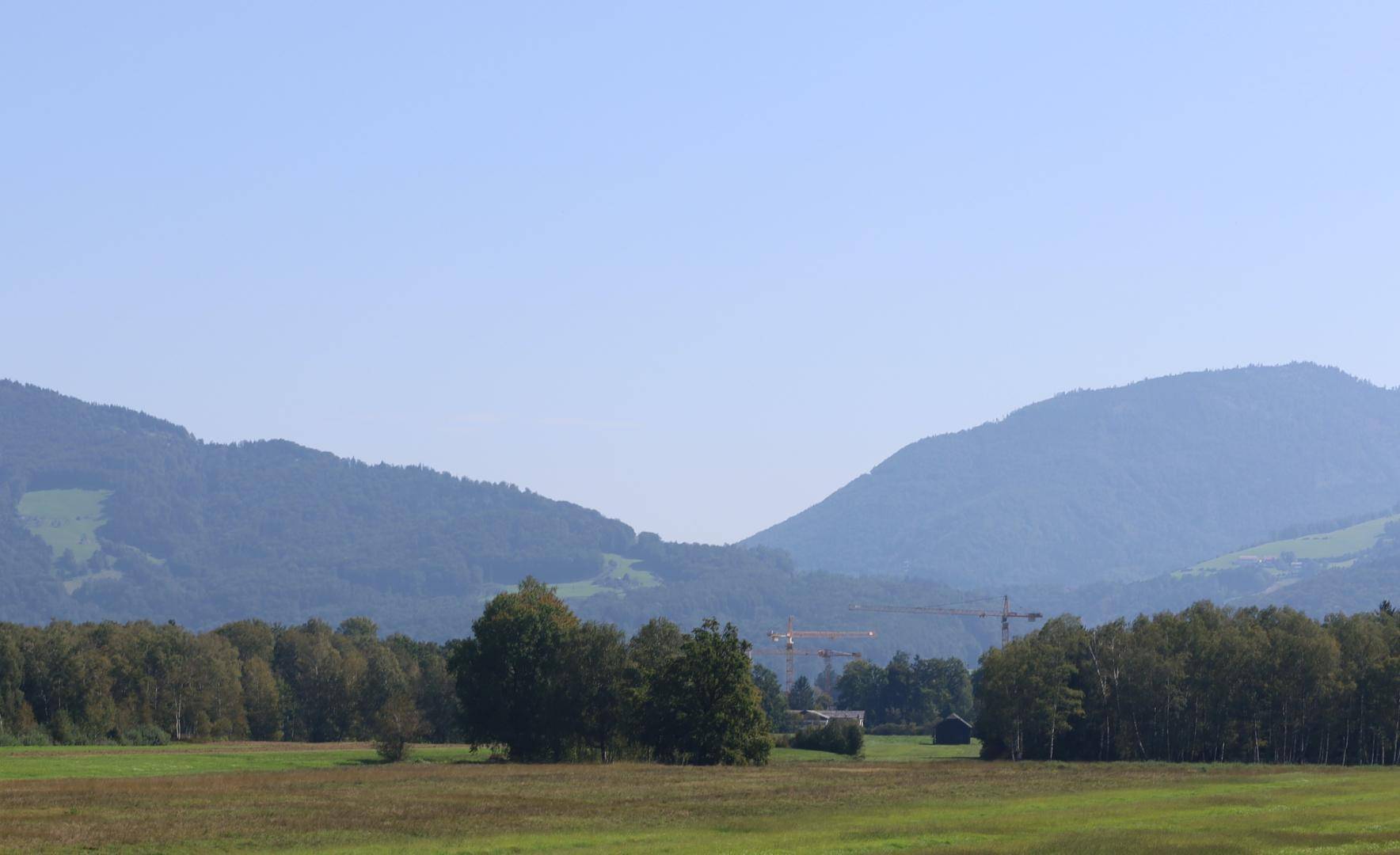Weitläufige Landschaft mit grünen Feldern, Wäldern und sanften Hügeln im Hintergrund.