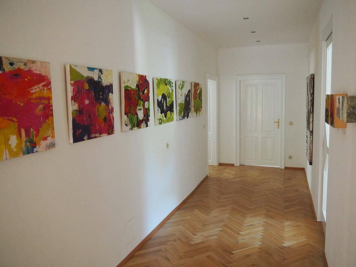 Heller Flur mit Fischgrätparkett, weißen Türen und farbenfrohen Kunstwerken an den Wänden.