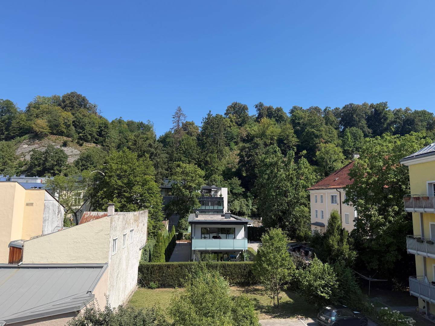 Weitläufiger Blick über eine grüne Wohngegend mit vielen Bäumen und Hügeln im Hintergrund.