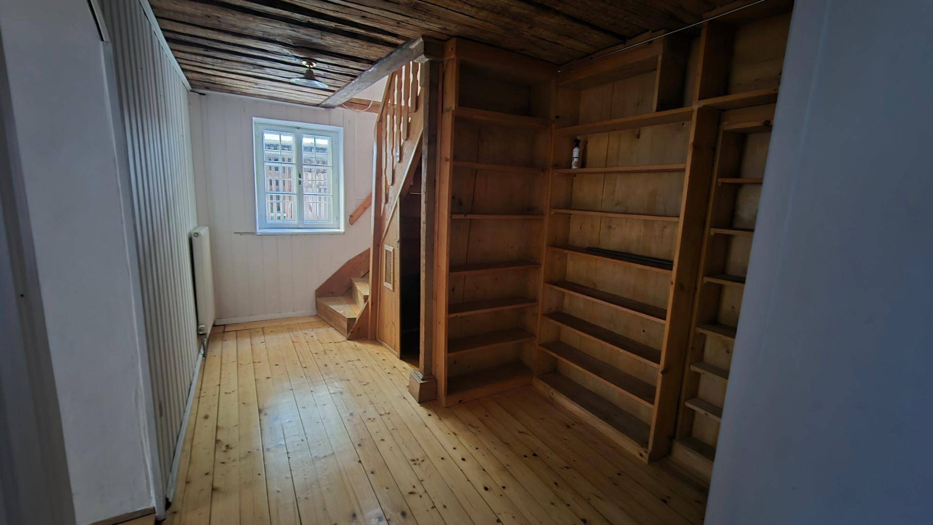 Raum mit Holzboden, eingebauten Holzregalen und einer Holztreppe, die in ein weiteres Stockwerk führt.