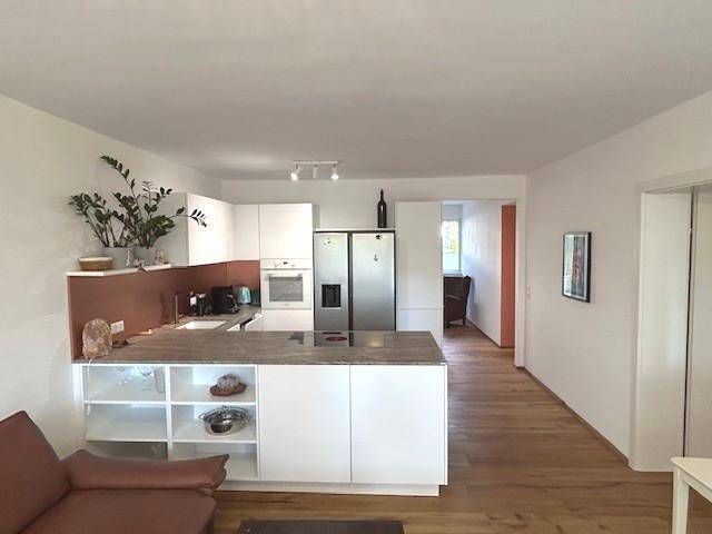 Moderne offene Küche mit weißen Schränken, Kücheninsel und Edelstahlgeräten, verbunden mit dem Wohnbereich.