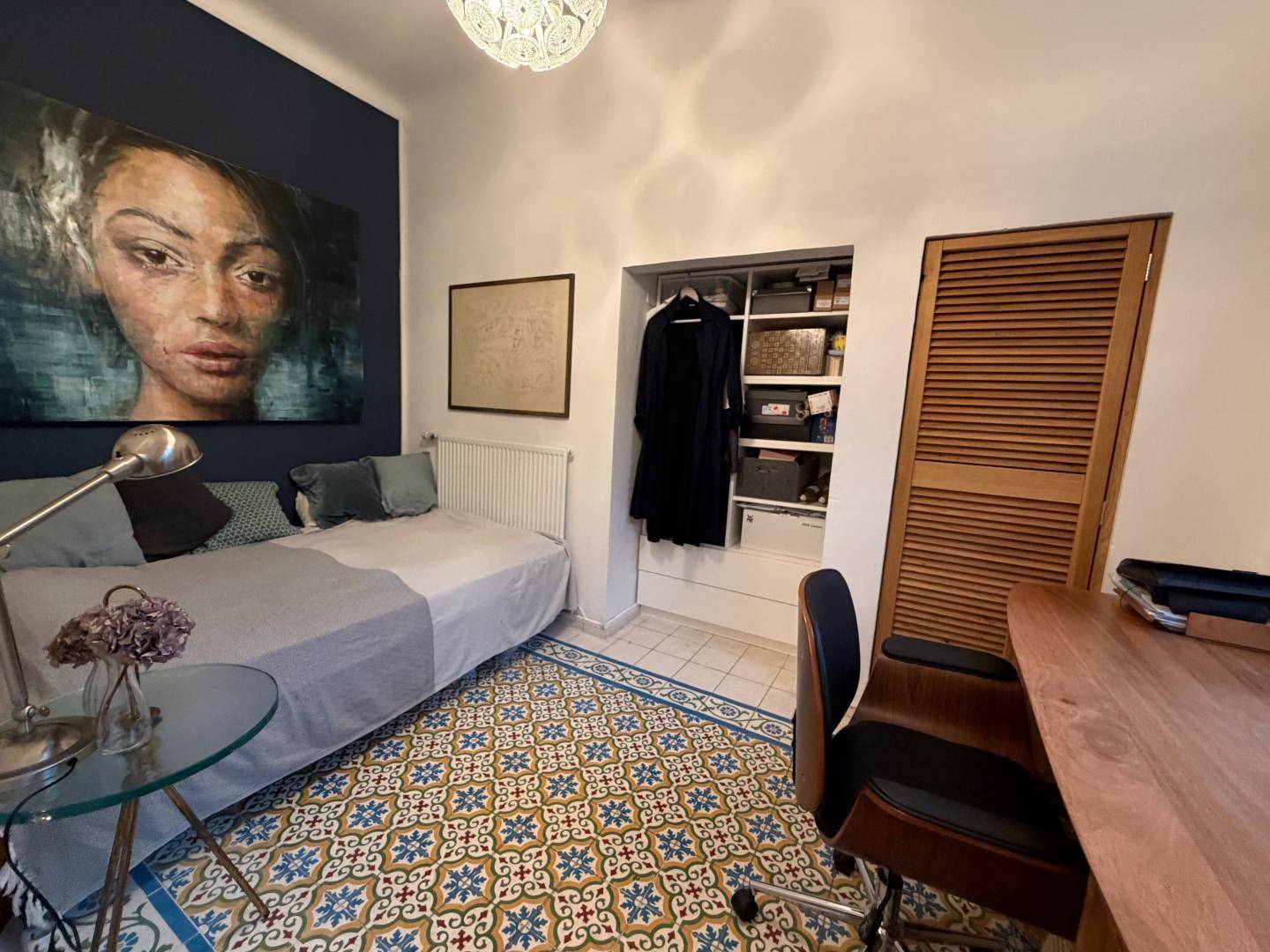 Schlafzimmer mit Tagesbett, farbenfrohem Wandbild und integriertem Stauraum, mit gemusterten Fliesen.