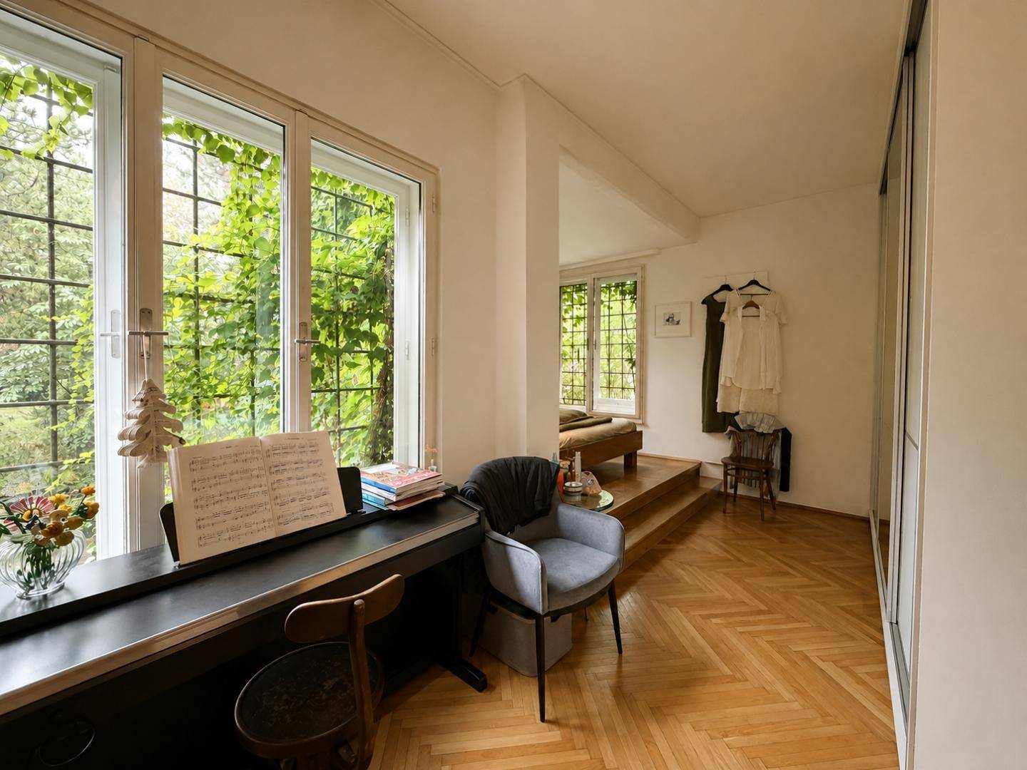 Schlafzimmer mit großen Fenstern und Blick ins Grüne, inklusive Klavier und erhöhtem Schlafbereich.