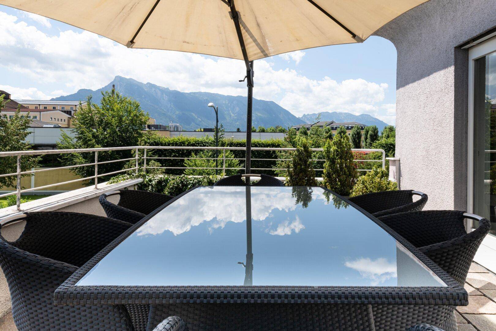 Geräumige Terrasse mit Korbmöbeln, Sonnenschirm und beeindruckendem Bergblick.