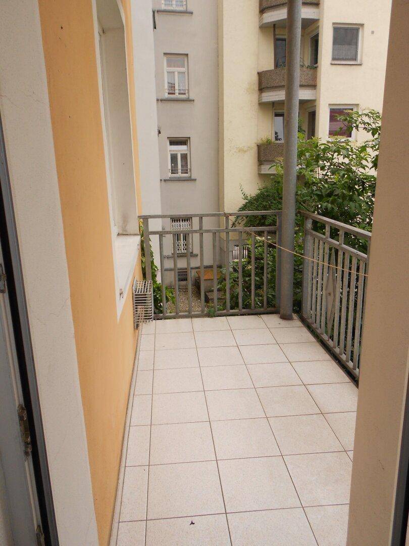 Kleiner Balkon mit Fliesenboden und Metallgeländer, umgeben von anderen Gebäuden.