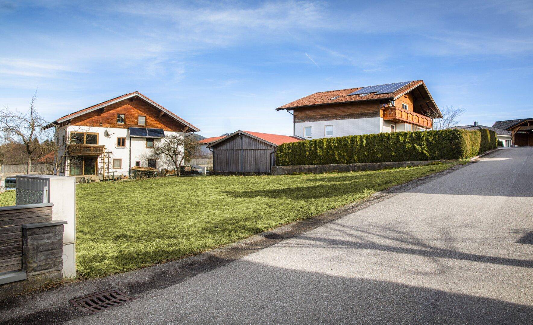 Zwei Wohnhäuser mit gepflegtem Rasen, Hecke und einer Zufahrtsstraße unter strahlendem Himmel.