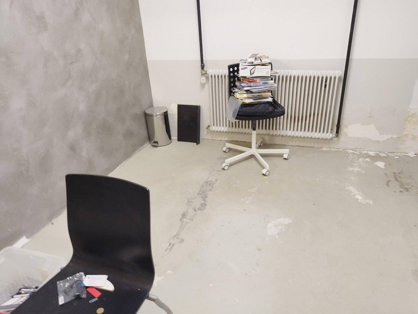 Einfacher Raum mit Betonboden, Heizkörper und einem Bürostuhl, ideal als Abstellraum.