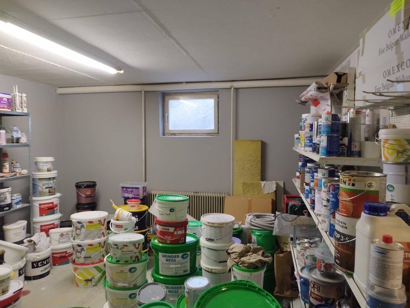 Lagerraum mit einem kleinen Fenster, gefüllt mit Farbeimern und Regalen an den Wänden.