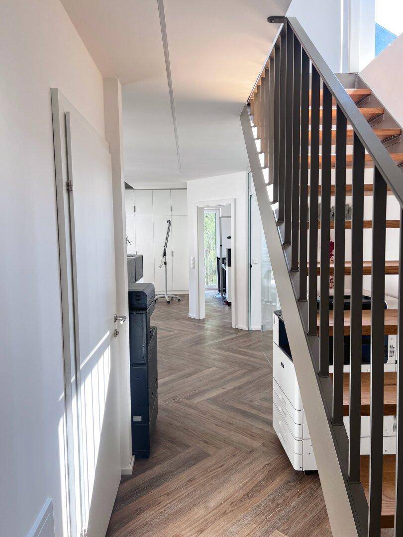Heller Flur mit eleganter Holztreppe und Fischgrätparkett, der zu weiteren Räumen führt.