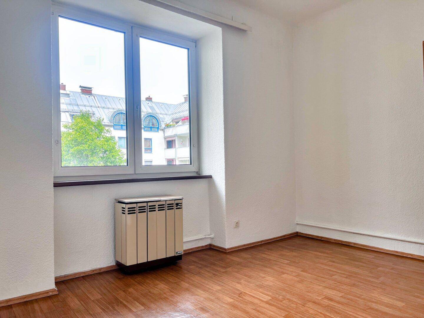 Heller Raum mit Holzfußboden, großem Fenster und Heizkörper.
