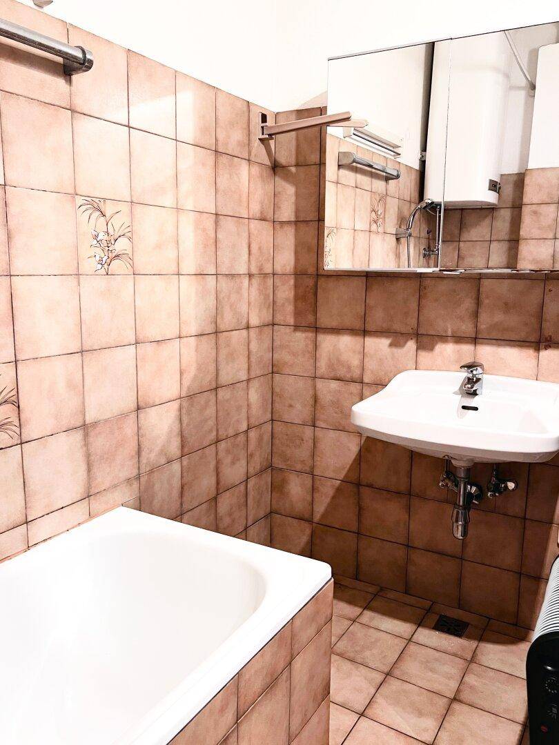 Badezimmer mit Badewanne, Waschbecken und braunen Fliesen im 80er-Jahre-Stil.