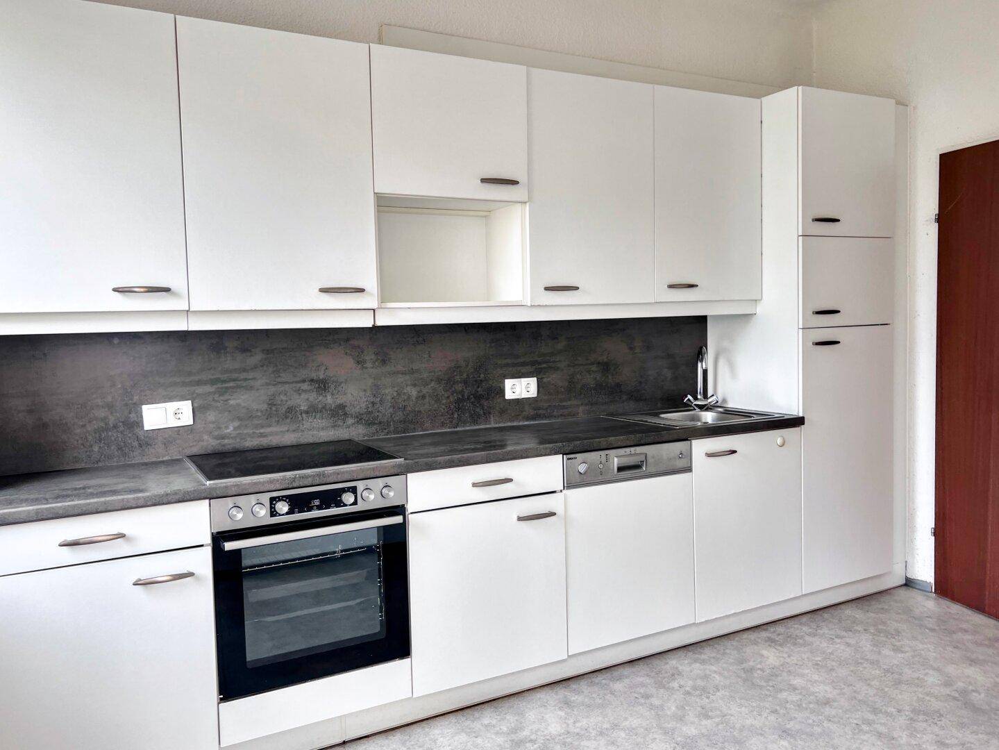 Moderne Einbauküche mit weißen Schränken, dunkler Arbeitsplatte und integrierten Geräten.