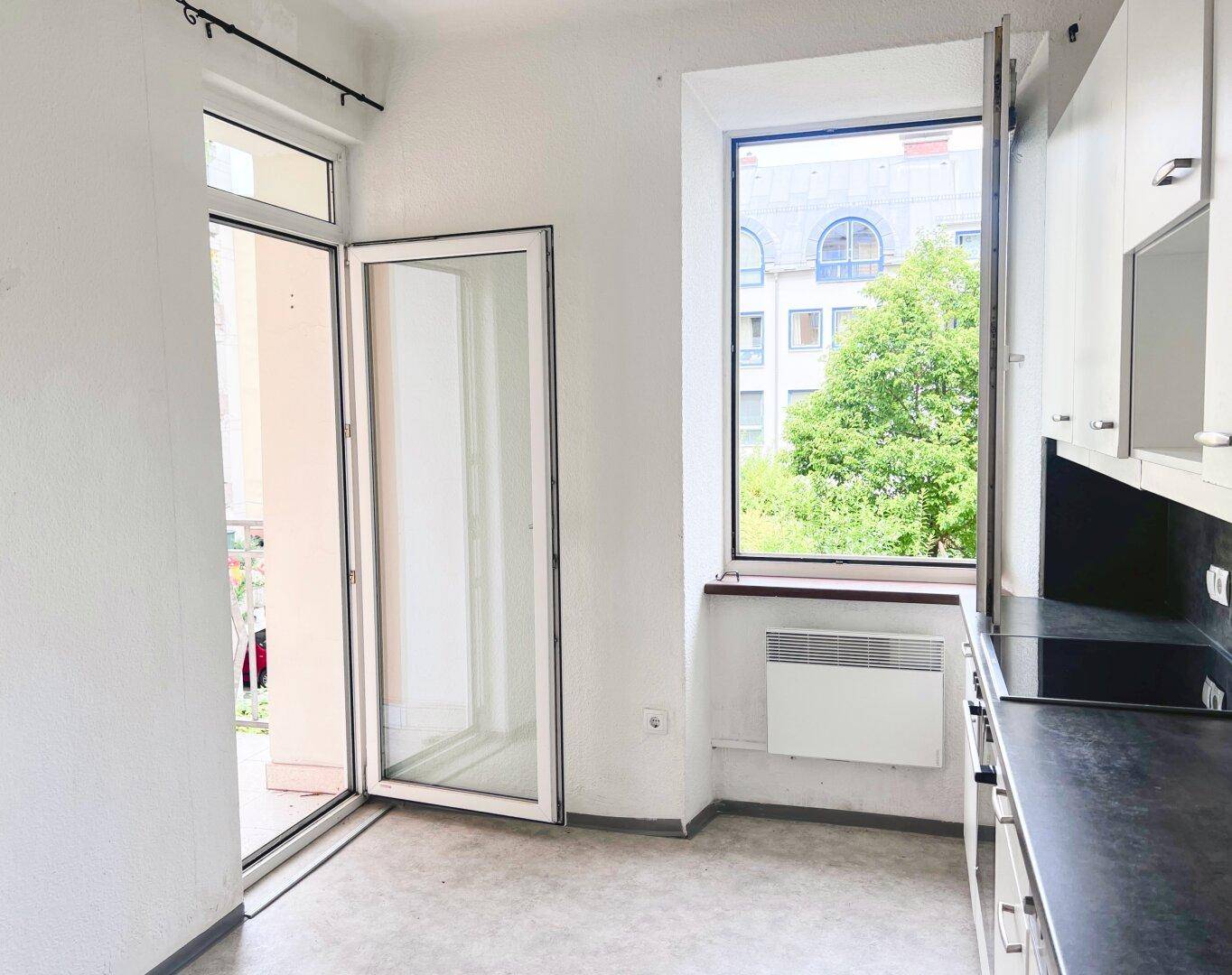 Küchenbereich mit Zugang zum Balkon, dunkler Arbeitsplatte und Fenster.